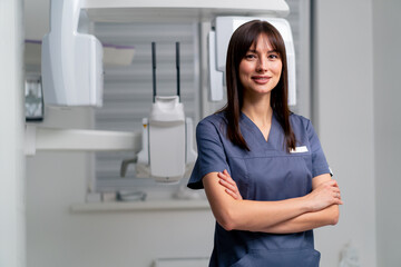 portrait of a beautiful young female doctor dentist or radiologist in uniform standing with crossed...