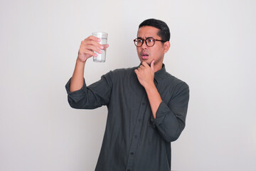 Adult Asian man looking to the glass of water that he hold with worry expression