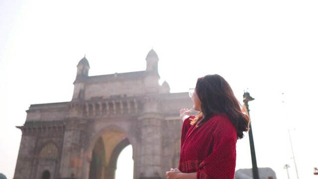Portrait of smiling Indian girl showing Gateway of India in Mumbai, India. Welcoming gesture of girl. Indian girl background. Beautiful smiling confident young Indian ethnic woman.