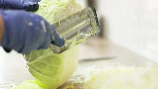 woman with blue gloves chopping cabbage on table with special cabbage shredder knife