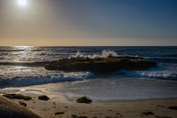 Fototapeta na wymiar 2023-12-14 A BACKLIT WAVE CRASHING ON THE SHORE OF A SMALL SAND BEACH IN LA JOLLA CALIFORNIA WITH A BRIGHT SUN REFLECTING OFF THE WATER