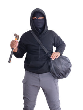 An unidentified male criminal wearing a black hoodie and covering his face, holding a hammer and carrying a large black bag. On a white background with cliping path. Thief.weapon, crime.