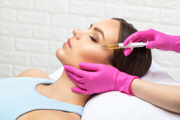 Cosmetologist makes rejuvenating anti wrinkle injections on the face of a beautiful woman. Female...