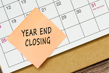 Year end closing text on sticky note and stuck to a calendar background.