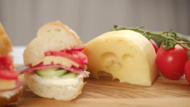 Close up of baguette sandwiches with salami, green cucumber, cheese and fresh tomatoes on wooden cutting board in home kitchen. Subway sandwiches. Food concept. Selective focus