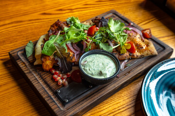 Chicken kebab with vegetables, greens and pita bread with sauce on a wooden plate