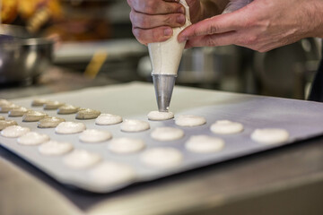 Mains d'un homme qui tient une poche à douille et qui fait des macarons 