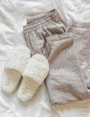 Homemade cotton trousers and soft fur slippers on a light background, top view