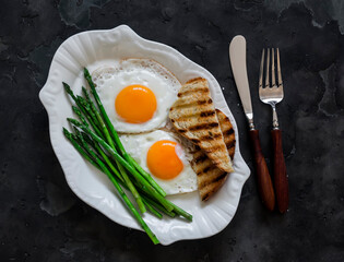 Simply breakfast, snack, brunch - fried eggs and asparagus on a dark background, top view