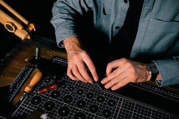 Top view of male hands. A tanner makes a black belt on a dark table and tools DIY instruction, production, business