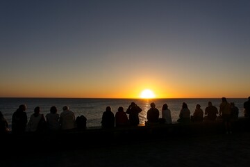 Rear view of a group of people silhouette on the beach at sunset against sun in Maspalomas, Gran Canaria, Spain