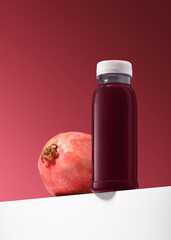 A plastic bottle with pomegranate juice and pomegranate fruit stand on a white podium. Red...