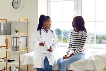 Poster Happy African American female doctor and patient discussing treatment. Young woman physician in white medical coat sitting on examination bed with young girl, talking about her therapy, giving advice © Studio Romantic