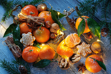 Tangerines mandarins with cinnamon, gingerbread, cookies, anise on a dish and on the wooden table, fir branches, decor sleigh and a light garland. Christmas card.