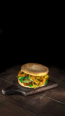 Hamburguer com carne, queijo derretido, alface e aneis de cebola sobre fundo de madeira