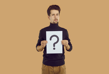 Doubting young man holding paper note with question mark. Portrait of puzzled thoughtful guy wearing casual style clothing showing question sign trying to solution problems, getting answers