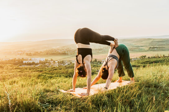 Two women practicing acroyoga on a hill at sunset
