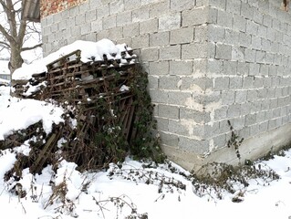 Old pallets of construction materials are piled up against the block wall and covered with snow.