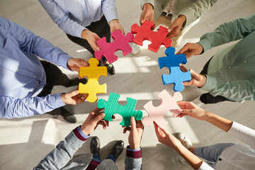 Obrazy na Plexi  Business team playing with puzzle. Group of young people connecting green, yellow, pink, red, blue pieces of jigsaw puzzle. People holding different jigsaw parts in hands. Teamwork concept background