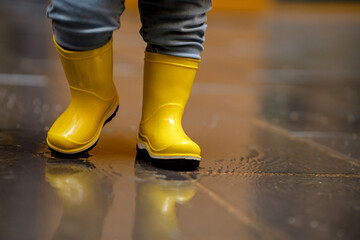 A child in yellow boots walks on wet asphalt
