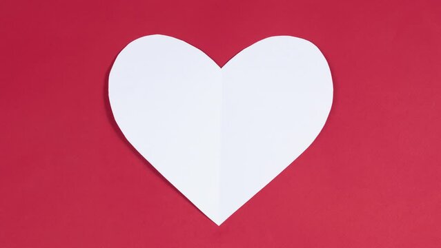 4k Big white heart flaps its wings. Symbol of love. Greeting card. Concept of valentine's holiday, wedding and other occasions to express love. Red background. Stop motion animation. Flat lay.