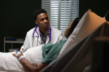 African female patient lying in a hospital bed is attentively listening to a young African doctor...