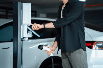 Young man travel with EV electric car to shopping center parking lot charging in downtown city...