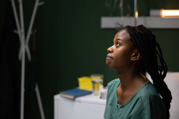 African patient in the hospital room sitting on the bed, looking upset and praying.