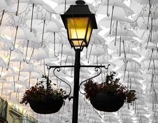candeeiro aceso numa rua decorada com guarda-chuvas.