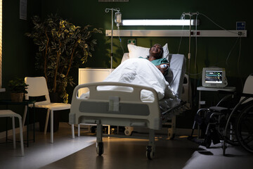 African woman lies in the hospital bed, curled up, feels pain in her stomach due to suspected gastritis.