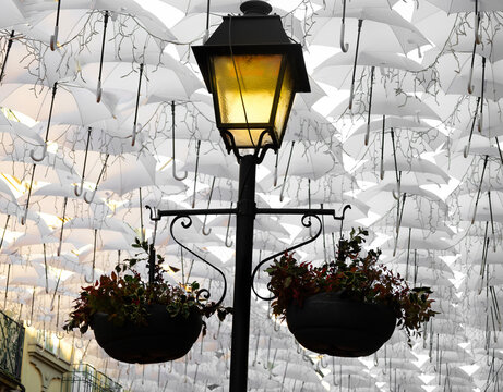 candeeiro aceso numa rua decorada com guarda-chuvas.
