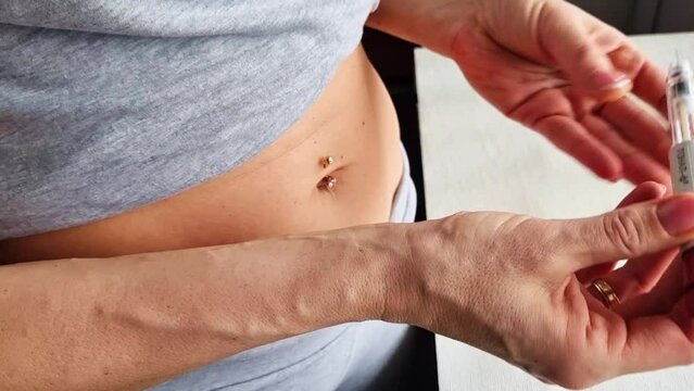 Close up footage of the woman with beautiful hands, preparing hormone medicine and injecting herself to the abdomen with pierced bellybutton. Family planning
