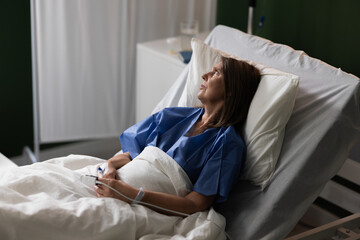 Woman of advanced age in hospital lies, gazing at the view outside.