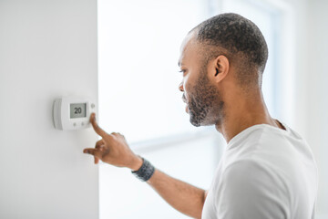 man choosing temperature on thermostat. Young focused guy pushing button home system.
