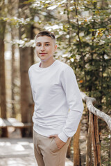 Close-up vertical portrait of a teenager in a white sweater and brown pants. Happy smiling teenager in summer park in sunlight. A beautiful child is looking at the camera in the clearing.