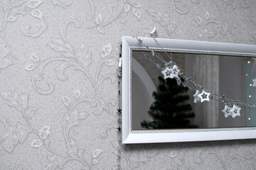 A mirror decorated with a garland and a reflection of a Christmas tree