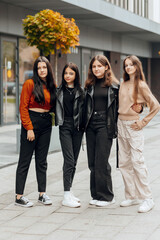 Fototapeta premium Group of smiling and happy teenage friends wearing casual clothes spending time together, posing and talking with each other near college building on autumn day.