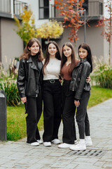 Group of smiling and happy teenage friends wearing casual clothes spending time together, posing and talking with each other near college building on autumn day.