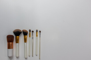 Make up brushes with white handles lined up in a row to the left on white background with copy space