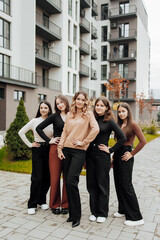 Fototapeta premium Group of smiling and happy teenage friends wearing casual clothes spending time together, posing and talking with each other near college building on autumn day.