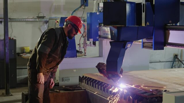 In production zone heavy industrial machinery cutting off the metal the blacksmith looking at the process he wearing special equipment and helmet
