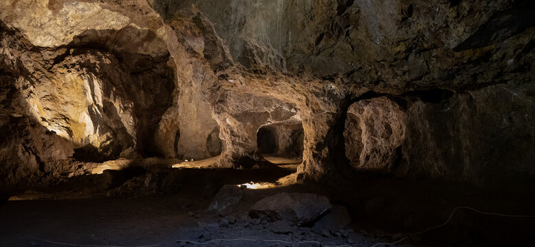 Dimly lit cave interior with rocky surfaces and shadows, creating a mysterious underground landscape.