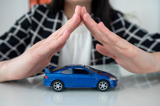 Small blue  toy car and female hand at office desk as insurance
