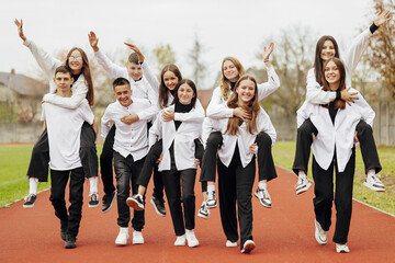 A group of many happy teenagers dressed in the same outfit having fun and posing in a stadium near...