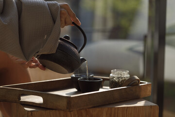 Black cast iron tea pot with herbal tea set up on wood tray. Traditional Asian Tea Set - iron teapot and ceramic teacups with green tea and tea leaves.