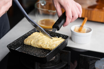 Chef man hands cooking Tamagoyaki or Tamago traditional Japanese Rolled Omelette recipe, made by...