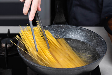 Professional chef cooks making Italian Capellini spaghetti pasta at modern kitchen gas stove in wok...