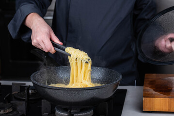 Professional chef cooks making Italian Capellini spaghetti pasta at modern kitchen gas stove in wok...