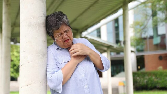 Elderly asian woman suddenly had serious heart attack and was unable to breathe stood holding her chest and felt pain in her chest was urgently helped by a young woman and taken to the hospital.