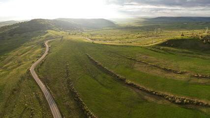 Obraz premium Aerial drone flight above a rural region in Transylvania at sunset. Grassy hills, sheep flocks, farms, storm clouds and sunlight create a beautiful countryside landscape. Romania